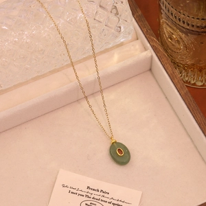 Detail of vintage gold necklace with oval green stone and small red gem on jewelry tray