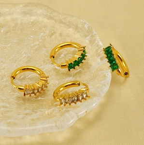 Détail de créoles en or 18K avec zircon émeraude et clair sur fond de satin chic