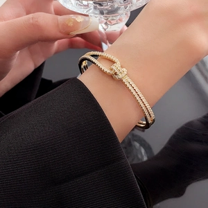 Detail of gold-finished knotted bracelet with cubic zirconia on a model with black suit