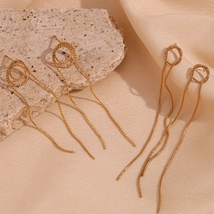 Close-up of gold snake chain tassel earrings on a textured stone and silk background