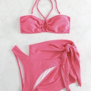 Pink ribbed three-piece bikini set with a matching sarong on a marble background