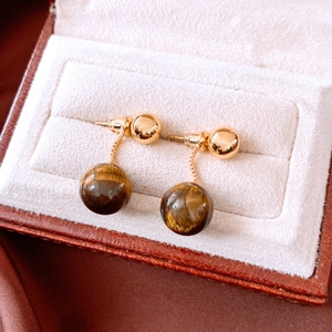 Macro view of 18k gold plated tiger eye stone drop earrings on white velvet background
