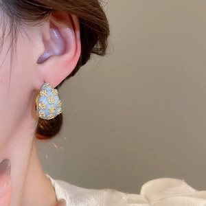 Close-up of model wearing a light blue enamel flower C-shaped earring with gold accents