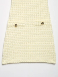 Detalle de tela de tweed amarillo claro con textura y botones metálicos dorados