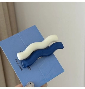 Close-up of white and blue wave-shaped hair clips in glossy resin with metal grips