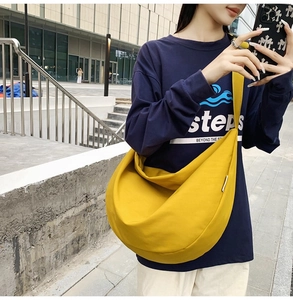 Close-up of bright yellow large canvas crossbody bag with wide shoulder strap on model