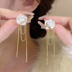 Detailed view of camellia flower earrings with gold tassel chains on a model's hand