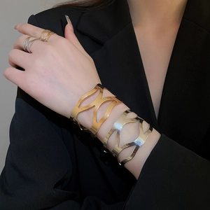Close-up of gold and silver hollow geometric bracelets and rings worn by a model