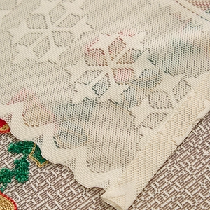 Macro shot of beige mesh lace tablecloth with floral patterns and red embroidery details