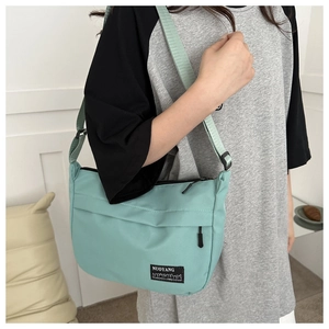 Detail of mint green nylon crossbody bag showing the front zip pocket and adjustable strap
