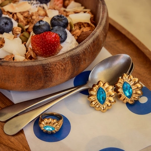 Close-up of gold flower-shaped earrings and ring set with oval blue gemstones