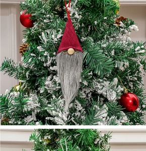 Detail of red knit hat Christmas gnome hanging on a decorated tree with snow