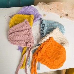 Flat lay of colorful knit baby hats with ear flaps and lace ties on a white table