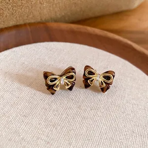 Elegant tortoise shell bow earrings with gold trim and crystal inlay on a rustic background