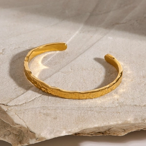 Minimalist golden wavy textured open cuff bracelet for women shown on a natural stone base