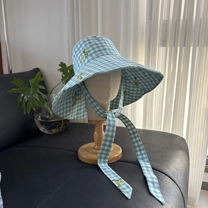 Detail of blue plaid sun hat with yellow floral embroidery and long side ribbons