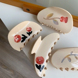 Detail of four beige hair claws with red floral patterns and small crystal accents
