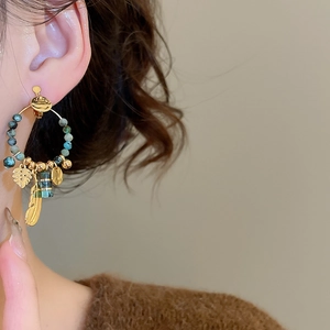 Detail of bohemian gold feather earrings with turquoise beads on model's ear