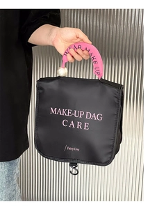 Detail of black makeup bag with pink handle, pearl accents and built-in hanging hook