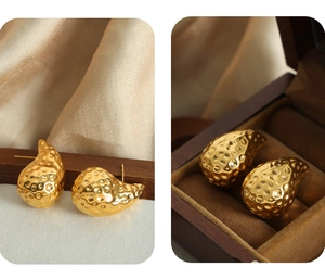 Detail view of gold-plated titanium earrings with hammered texture on a wooden stand