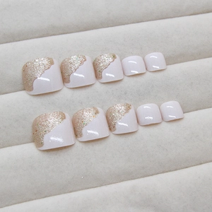 Pink shimmering fake toenails with golden glitter waves set on white display tray