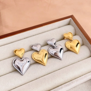 Close-up of gold and silver heart drop earrings displayed in a beige jewelry box