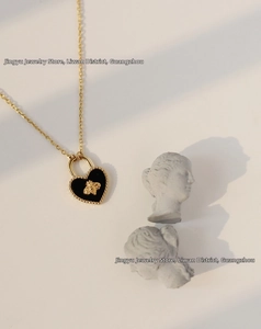 Detail of a 18K gold plated necklace featuring a black heart lock with a golden bee motif