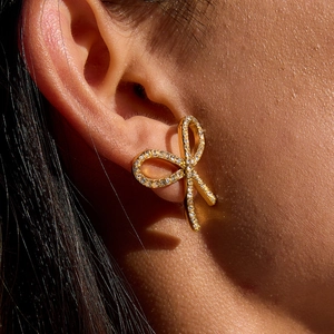 Golden bow earrings with sparkling white crystals shown on model in natural light