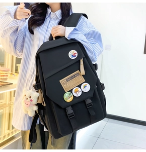 Detail of black nylon school backpack featuring cute badges and a plush bear pendant charm
