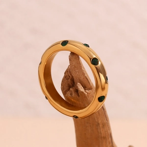 Detail eines 18K vergoldeten Rings mit grünen Zirkonen auf einem Stück Naturholz