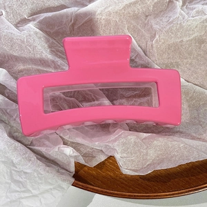 Detailed view of a bright pink rectangular hollow hair claw clip on a wooden display