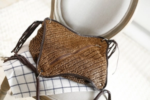 Détail d'un sac bandoulière en paille tressée marron avec de longs pompons et fermeture