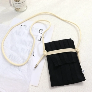 Detailed view of black pleated knitted phone bag with beige adjustable shoulder strap