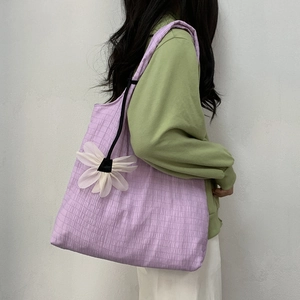 Detail of purple pleated canvas tote bag with white flower charm on a casual model