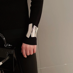 Close-up of a wide irregular silver cuff bracelet worn over a black knit sleeve