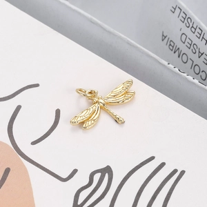 Detailed close-up of a 18K gold plated dragonfly pendant with textured wings on a book