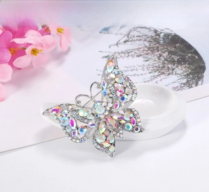 Close-up of vintage silver butterfly brooch with colorful AB rhinestones on a ceramic dish