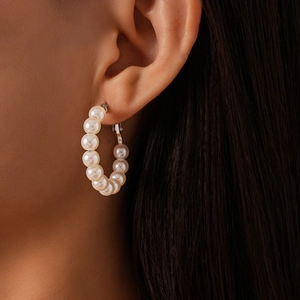 Macro side view of white faux pearls on a silver hoop earring worn on the ear model