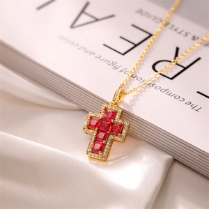Close-up of golden cross necklace with red gemstone on white silk background