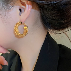 Detail of elegant gold woven hoop earring with intricate textured metal wire design