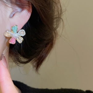 Detail of flower stud earring with green enamel, crystals, and pearl on model