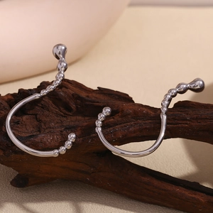 Macro view of silver streamlined ear cuffs with bead details on a textured wood base