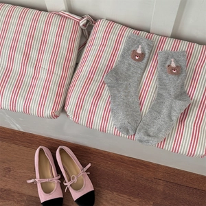 Detail view of gray teddy bear crew socks on a striped cushion with ballet shoes