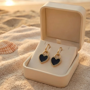 Close-up of golden heart earrings with black enamel on a sunset beach background