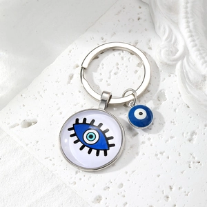 Detail of silver Evil Eye keychain with blue glass pendant on a white textured stone surface
