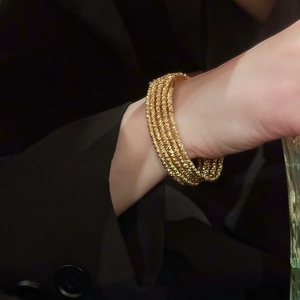 Close-up of a gold-plated multi-layered beaded bracelet worn with a black suit