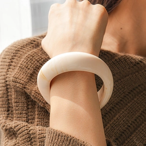 Detail of wide cream resin cuff bracelet worn with a brown knit sweater