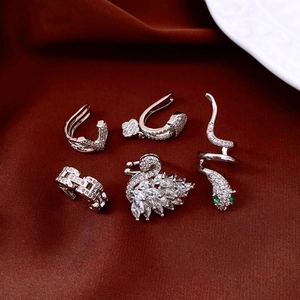 Detailed view of silver swan and snake ear cuffs with green zircon on red velvet