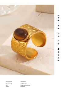 Detail of hammered gold ring with oval brown gemstone on a beige travertine background