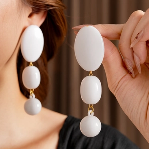 Detail shot of white beaded geometric earrings with gold links worn by a model